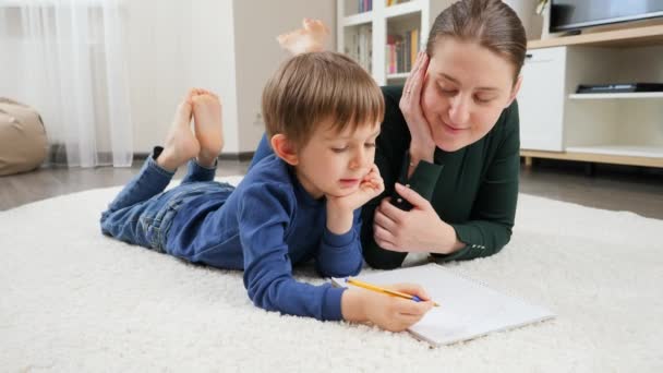 Genç bir anne evde ders veriyor ve oğlunun ödevlerini yapmasına yardım ediyor. Aile eğitimi, çocuk gelişimi ve mutlu ebeveynlik kavramı. - Video, Çekim
