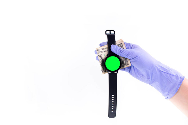 Πράσινη οθόνη Smart ρολόι στο χέρι στο γάντι καουτσούκ κρατώντας χρήματα με λευκό φόντο. Χώρος για κείμενο - Φωτογραφία, εικόνα
