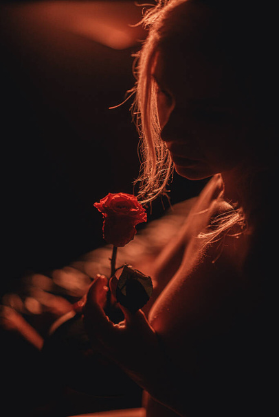 gyönyörű meztelen fiatal lány pózol egy vörös rózsa az ágyon - Fotó, kép
