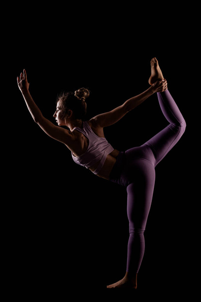 Fit girl practicing yoga in a studio. Half silhouette side lit fitness model. - Photo, Image
