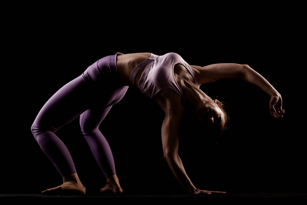 Fit girl practicing yoga in a studio. Half silhouette side lit fitness model. - Photo, image