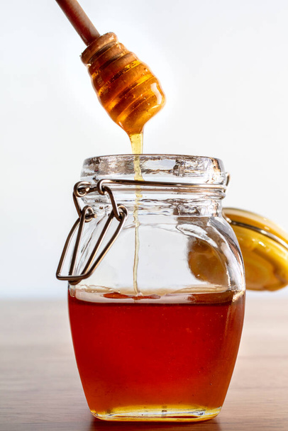 Перемешивая палку в банке с золотисто-сладким медом на верхушке деревянного стола - Фото, изображение