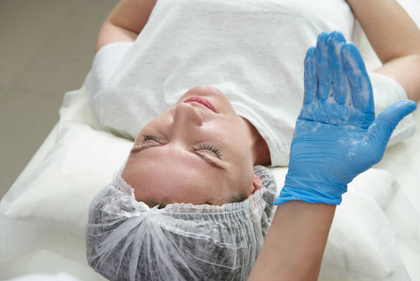 Νεαρή γυναίκα κάνει αφρόλουτρο μασάζ στο πρόσωπο. κοσμητολόγος εφαρμογή κρέμα ή αφρό στο γυναικείο πρόσωπο σε καθαρό δέρμα - Φωτογραφία, εικόνα