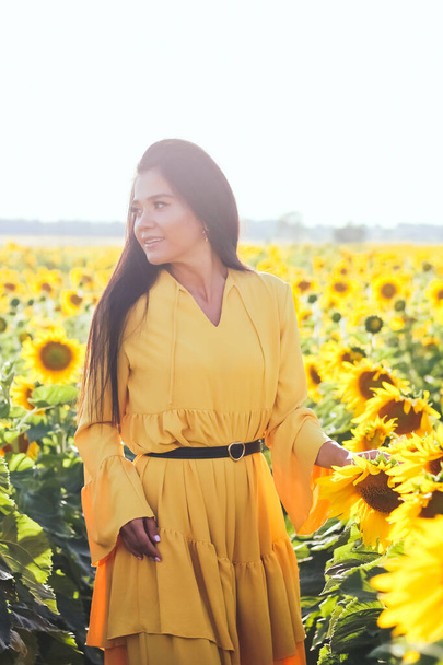 A brunette woman in a yellow dress on the field with sunflowers. Orange dress. - Photo, Image