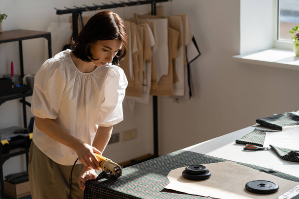 Atelier business owner woman tailor designer work in studio cut material for patterns with cutter - Fotografie, Obrázek