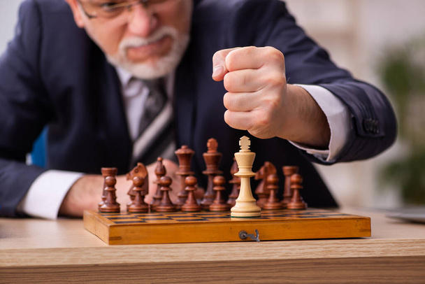 Vecchio dipendente maschio che gioca a scacchi sul posto di lavoro - Foto, immagini