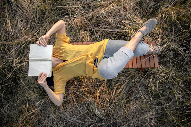 Chica con estilo con un libro en sus manos se encuentra entre la hierba en la naturaleza. - Foto, Imagen