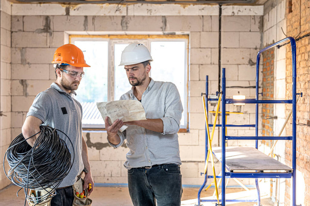 Dois engenheiros construtores conversando no canteiro de obras, engenheiro explicando um desenho para um trabalhador. - Foto, Imagem