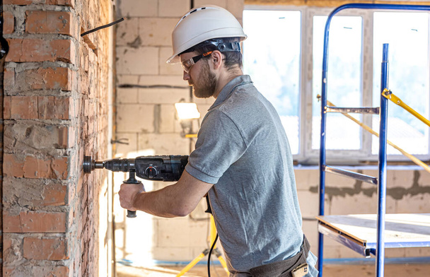 Handyman at a construction site in the process of drilling a wall with an perforator. - Photo, image