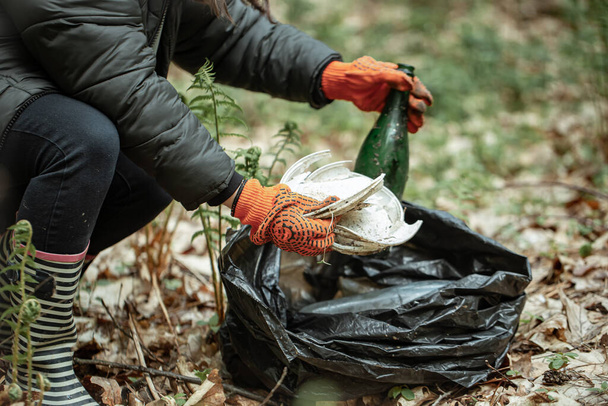 Добровольча дівчина зі сміттєвим пакетом очищає сміття в лісі
. - Фото, зображення