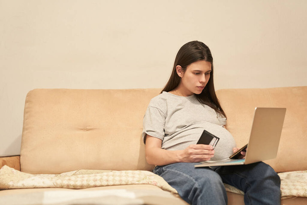 Mujer embarazada en casa con teléfono está sentado con el ordenador, compras en línea - Foto, imagen