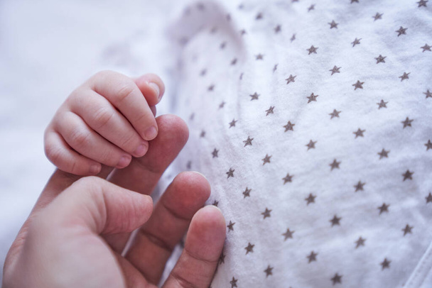 Moederhand houdt baby hand vast. Een maand oud. Concept van liefde en zorg - Foto, afbeelding