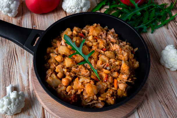 Homemade chicken stew with vegetables, potato, onion, carrot, cauliflower, pepper with tomato sauce, garlic and herbs in a frying dish on wooden table. Rustic food on wooden background - Photo, Image