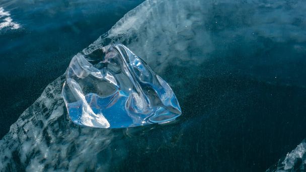 Glänzende Eissplitter, Nahaufnahme, Detail. Blendung der Sonne an den Rändern. Ein Riss ist in der Tiefe des zugefrorenen Sees zu sehen. Baikal - Foto, Bild