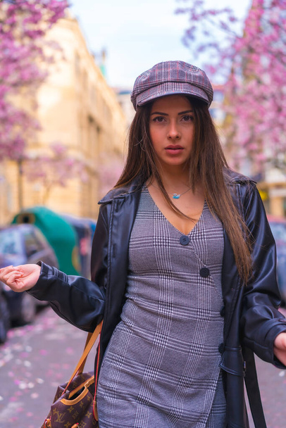 Street Style in the city, brunette Caucasian girl in a leather jacket and a beret in the city with the flowered trees in spring - Foto, imagen