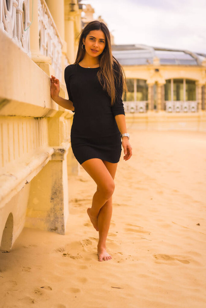 Lifestyle, πορτρέτο μιας νεαρής μελαχρινής Καυκάσιας γυναίκας με ένα κοντό μαύρο φόρεμα σε μια παραλία που απολαμβάνει τις καλοκαιρινές διακοπές - Φωτογραφία, εικόνα