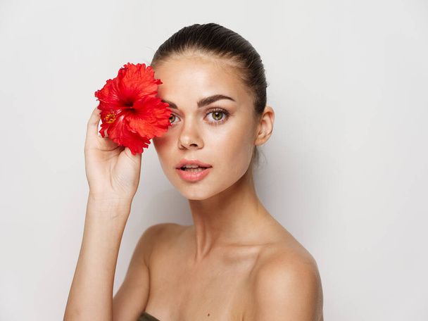 όμορφη γυναίκα γυμνοί ώμοι κόκκινο λουλούδι κοντά καλλυντικά προσώπου - Φωτογραφία, εικόνα
