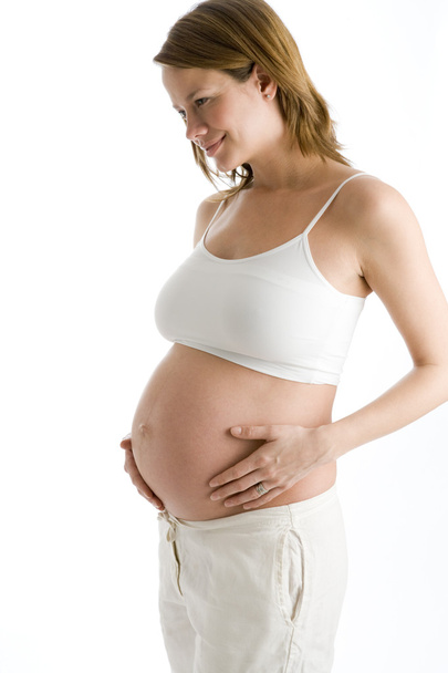 Pregnant woman holding exposed belly smiling - Фото, изображение