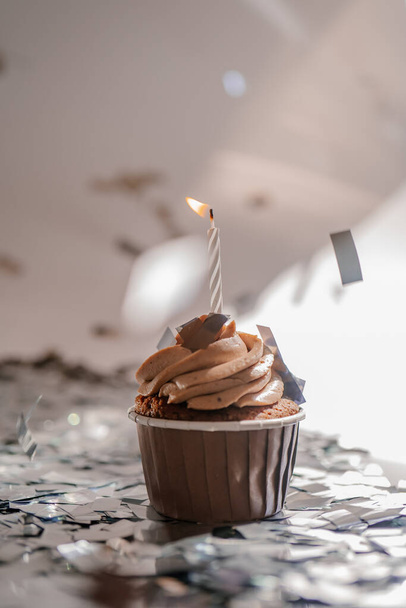 A cupcake with a candle stands on a white background with a shadow. - Φωτογραφία, εικόνα