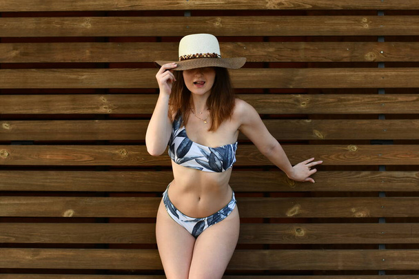 Mooie jonge vrouw in stijlvol zwempak poserend op houten achtergrond. Zomer levensstijl.  - Foto, afbeelding