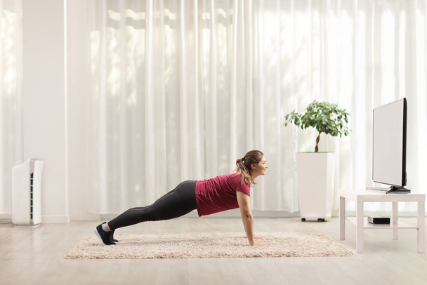 Young woman doing plank exercises in front of a tv at home - Foto, immagini