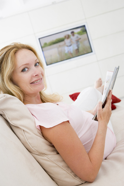 Pregnant woman reading magazine with television in background sm - Photo, Image