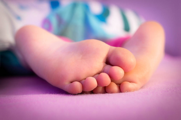 ベッドのカバーの下で眠っている赤ん坊の足 - 写真・画像