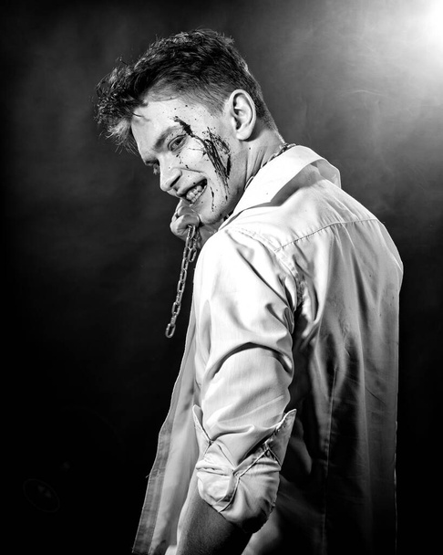 Black and white portrait of a maniac with blood on his face on a dark background - Φωτογραφία, εικόνα
