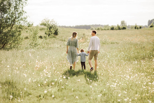 familia feliz caminando en el prado de flores florecientes por detrás, papá mamá e hijo, foto vista trasera - Foto, Imagen