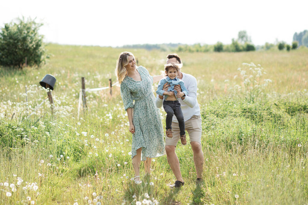 Photo of family enjoying summer day on flower meadow, parents love their little son 3 year - Foto, imagen