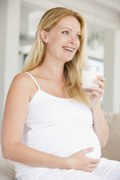 Pregnant woman with glass of milk smiling - Фото, изображение