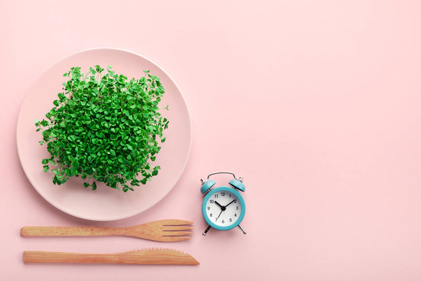 Relógio despertador, talheres e prato com vegetação em rosa. Conceito intermitente de jejum, almoço e dieta. - Foto, Imagem