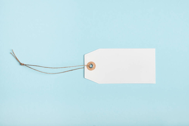 Blank paper price tag with a knotted string on a blue background - Fotó, kép