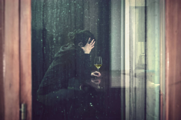 einsame betrunkene Frau zu Hause, Spiegelung durch das Fenster einer alkoholisierten jungen Frau an einem regnerischen Tag  - Foto, Bild