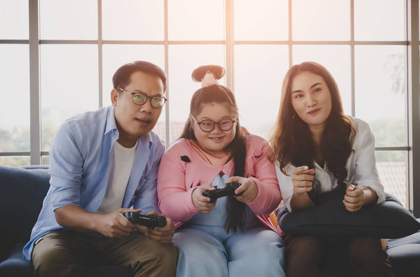 Down Sendromlu Asyalı Aile, Otizm ve pozitif aile kavramı için evdeki oturma odasında video oyunu oynuyor.. - Fotoğraf, Görsel