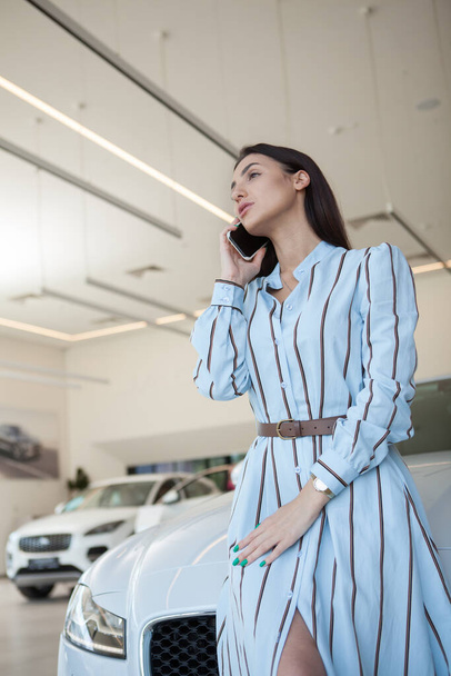 Vertical portrait of an elegant woman talking on her mobile phone at car dealership - Foto, imagen