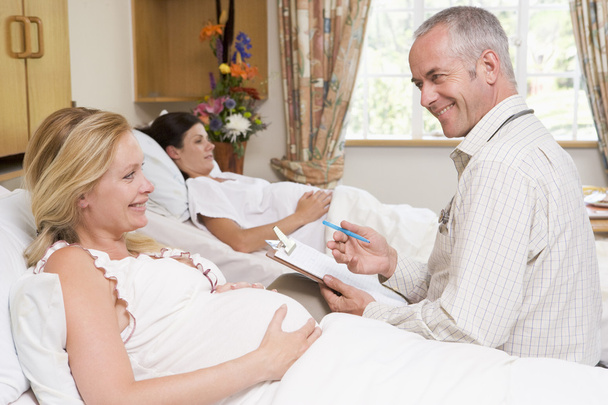 Doctor hablando con la mujer embarazada sosteniendo el gráfico y sonriendo
 - Foto, Imagen