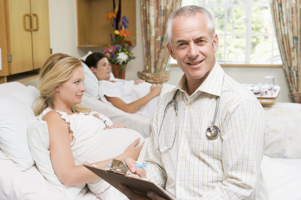 Doctor sitting by pregnant women holding chart and smiling - Фото, изображение