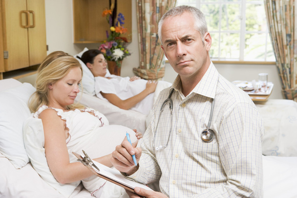 Doctor sitting by pregnant women holding chart - 写真・画像