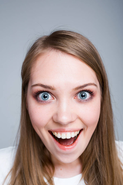 Close up photo. Portrait of a young happy girl who is surprised opening her mouth and looking into the camera - Фото, изображение