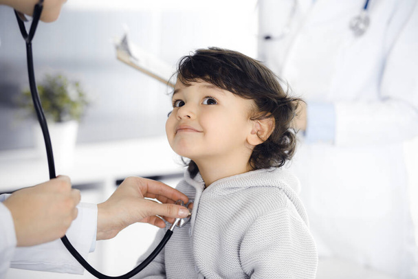 Woman-doctor examining a child patient by stethoscope. Cute arab toddler at physician appointment. Medicine concept - Foto, Imagem