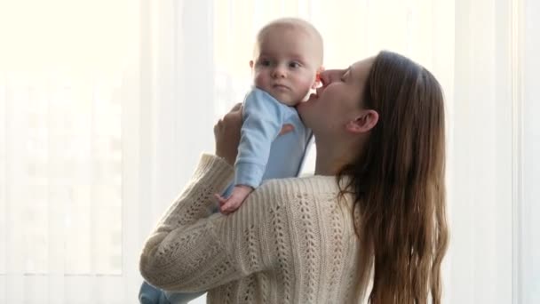 幸せな笑みを浮かべて母親の手に彼女の小さな赤ちゃんの息子を保持し、頭の中でキス。家族の幸せと子育ての概念 - 映像、動画