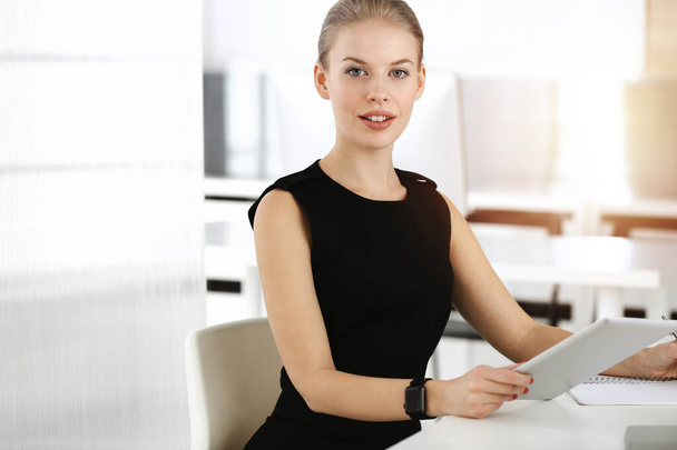 Young blond businesswoman dressed in black dress looks perfect in sunny modern office. Business people concept - Фото, зображення
