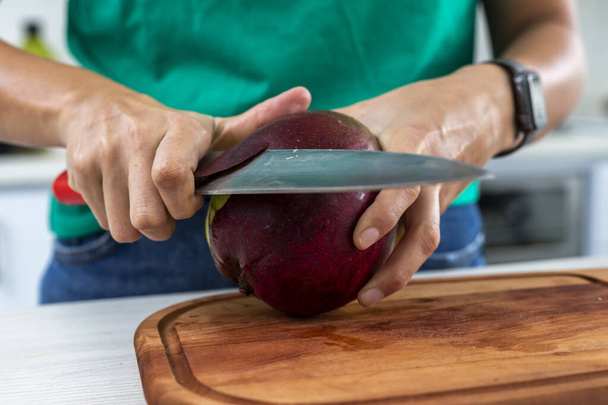 nő vágás egy mangó a konyhában egy fa fórumon - Fotó, kép