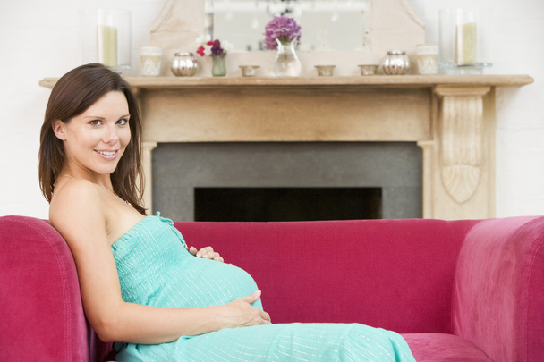 Terhes nő ül a nappaliban mosolyogva - Fotó, kép