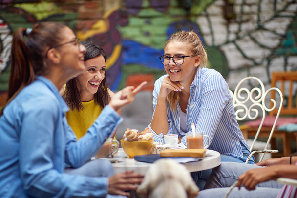 group of young adult caucasian female friends talking and laughing in outdoor cafe, drinking coffee - Fotografie, Obrázek