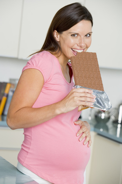 Pregnant woman in kitchen with large chocolate bar smiling - Fotoğraf, Görsel