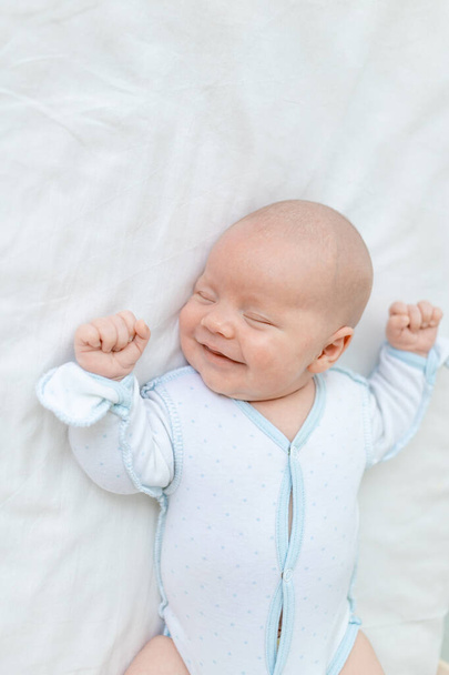 sonriendo o riendo en un sueño, un bebé recién nacido duerme durante siete días en una cuna en casa en una cama de algodón, de cerca - Foto, Imagen