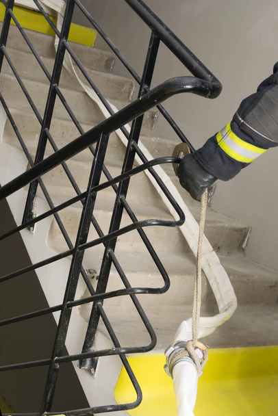 the fireman's hand secures the fire line to the railing in the residential entrance - 写真・画像