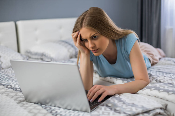 Upset woman using laptop while spending time in her bedroom. - Fotó, kép